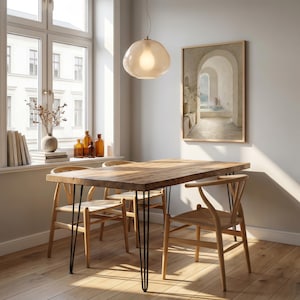 May include: A wooden dining table with black hairpin legs and four wooden chairs. A light fixture hangs above the table. A framed painting and a window are in the background. A vase of dried flowers and books sit on the windowsill. The table is approximately 150 cm long.