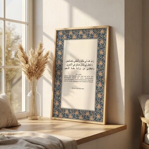May include: A framed print featuring Arabic calligraphy and English text. The frame is a light wood color, and the print has a floral border in blue and orange. The text includes the phrase "My Lord" and a quote from Surah Ash-Shu'ara.