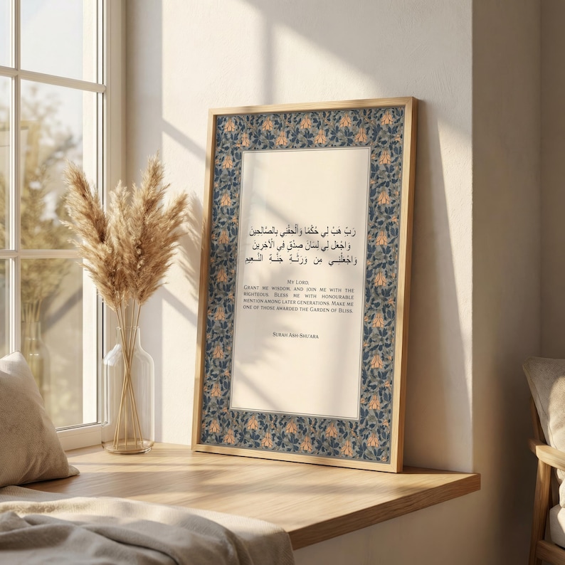 May include: A framed print featuring Arabic calligraphy and English text. The frame is a light wood color, and the print has a floral border in blue and orange. The text includes the phrase "My Lord" and a quote from Surah Ash-Shu'ara.