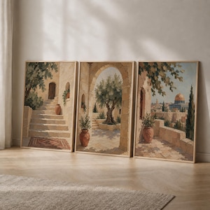 May include: A set of three framed wall art prints depicting Mediterranean-style stone architecture. The scenes feature stone staircases, arched doorways, potted plants, olive trees, and a distant view of a golden-domed building under a blue sky.