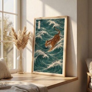 May include: Framed art print featuring a tiger in a teal ocean with white waves. The tiger has orange and black stripes. The artwork is in a light wood frame and is displayed on a wooden ledge near a window.