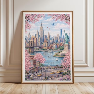 Op de afbeelding: Een ingelijste kunstdruk met een levendig stadsbeeld van New York City, met het Empire State Building, het Vrijheidsbeeld en de Brooklyn Bridge. Roze kersenbloesems omlijsten de sc&egrave;ne, met gele taxi's en voetgangers op straat.