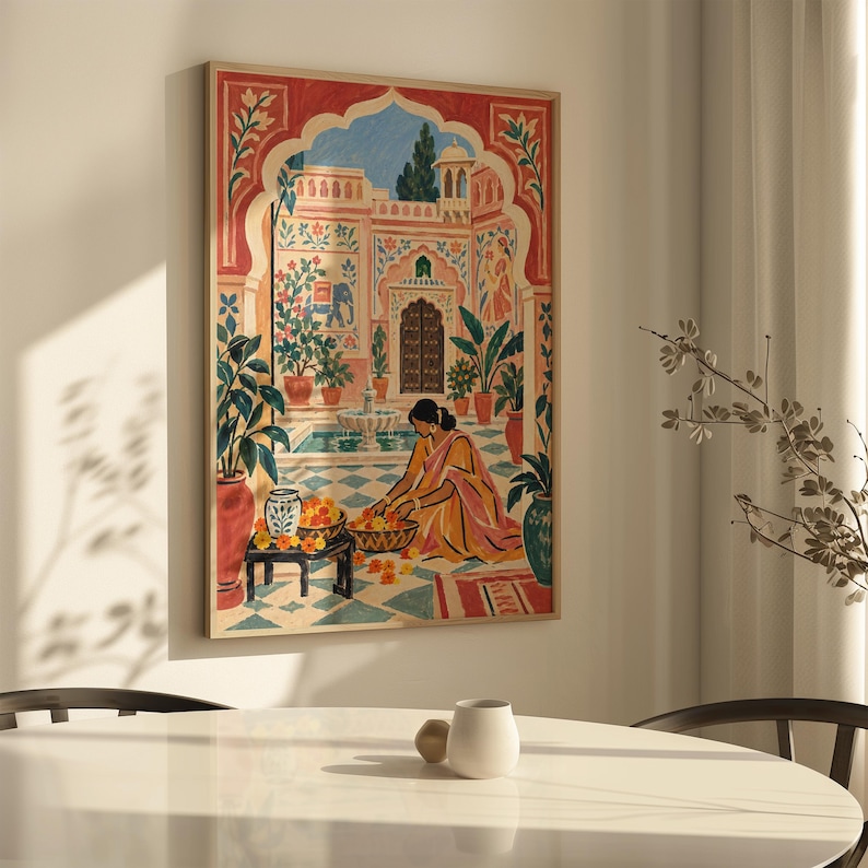 May include: A rectangular framed wall art print featuring a colorful illustration of a person in a yellow and pink sari sitting in a courtyard with a fountain, potted plants, and an arched entryway, rendered in warm tones of red, orange, and blue.
