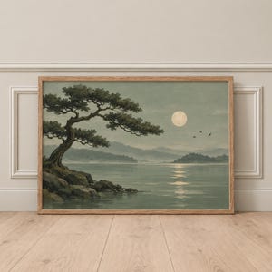 May include: A framed landscape print featuring a gnarled pine tree on a rocky shoreline overlooking a calm lake under a full moon. The scene is rendered in muted sage green and gray tones, with three small birds flying near the pale moon.