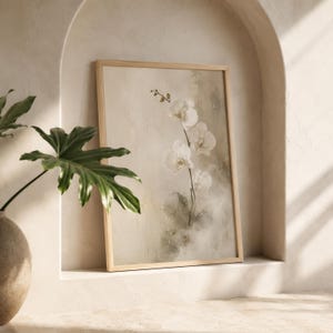 K&ouml;nnte beinhalten: Ein gerahmter Kunstdruck mit einem zarten wei&szlig;en Orchideenzweig vor einem weichen, neutralen und strukturierten Hintergrund. Das Kunstwerk befindet sich in einem hellen Holzrahmen und zeigt feine Pinselstriche sowie gedeckte Beige- und Cremet&ouml;ne.
