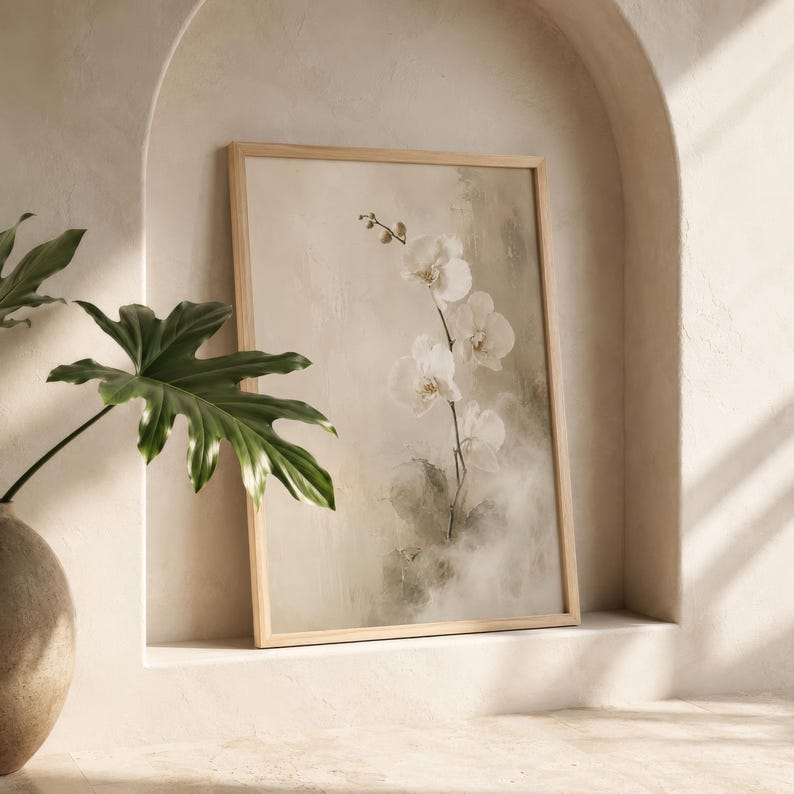 K&ouml;nnte beinhalten: Ein gerahmter Kunstdruck mit einem zarten wei&szlig;en Orchideenzweig vor einem weichen, neutralen und strukturierten Hintergrund. Das Kunstwerk befindet sich in einem hellen Holzrahmen und zeigt feine Pinselstriche sowie gedeckte Beige- und Cremet&ouml;ne.