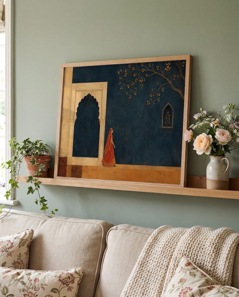 May include: A framed rectangular wall art print featuring a dark blue background with a person in a vibrant orange garment walking past a light-coloured stone archway. A golden tree branch extends from the top right corner near a small window.