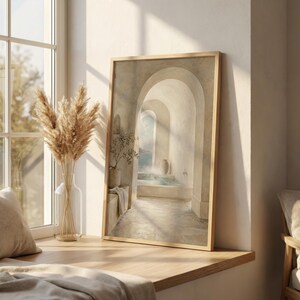 May include: A framed print depicting an arched hallway with a pool of water, a vase, and a plant. The print is in a light wooden frame and is set on a wooden windowsill. A vase of dried flowers sits next to the print.