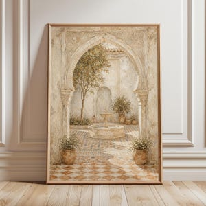 Op de afbeelding: Een ingelijste aquarelprint toont een gewelfde binnenplaats met een fontein, potplanten en een boom. Het kunstwerk heeft een warm kleurenpalet van beige, bruin en oranje, met een geblokte tegelvloer. De print wordt weergegeven op een houten vloer tegen een witte muur.