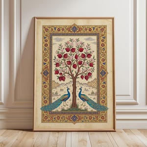 Op de afbeelding: Een ingelijste kunstdruk met een gestileerde boom vol rode granaatappels en roze bloesems. Twee pauwen staan aan de voet van de boom. Het kunstwerk is omlijst met een sierlijke rand in goud, rood en blauw.
