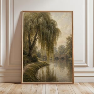May include: A framed landscape painting depicts a serene waterside scene. A large weeping willow tree dominates the left, its branches cascading towards the water. A stone bridge arches over the water in the distance, with trees and a soft, overcast sky.