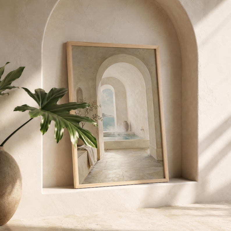May include: A framed print showing a tranquil architectural scene with arched doorways and a coastal view. The artwork uses a muted palette of beige, white, and blue, and has a wooden frame. A potted plant with large green leaves is in the foreground.