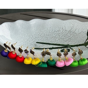 Może przedstawiać: Kolekcja kolorowych kolczyków z frędzlami. Każdy kolczyk ma żywą jedwabną frędzlę w odcieniach fioletu, czerwieni, żółci, zieleni i różu. Kolczyki mają złote metalowe akcenty z motywem liścia.