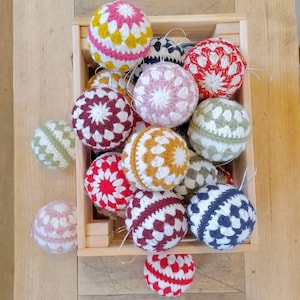 May include: A wooden crate filled with crocheted Christmas ornaments in various colors and patterns, including red, white, blue, green, pink, and yellow.