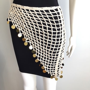 May include: Cream-colored, crocheted hip wrap with a net-like design. The wrap is adorned with gold-colored circular sequins along the bottom edge. The garment is displayed on a mannequin, showcasing its draped style and texture.