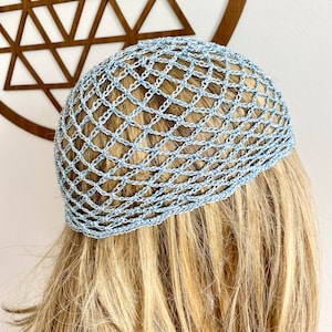 Può includere: Un copricapo all'uncinetto azzurro con un design a rete. Il copricapo è realizzato con un filato azzurro con un motivo sottile. L'articolo è mostrato su una persona con i capelli biondi.