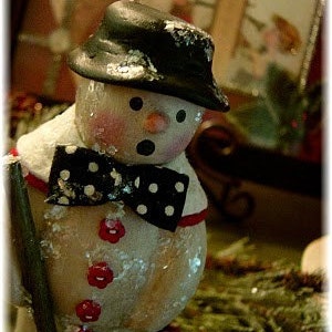 May include: A white snowman figurine with a black top hat and a black and white bow tie. The snowman is holding a stick in its right hand.