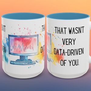 Peut inclure: Une tasse à café en céramique blanche avec un bord et une poignée bleus. La tasse présente une illustration aquarelle d'un ordinateur avec un graphique à l'écran et le texte "That wasn't very data-driven of you."