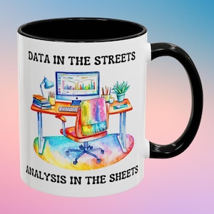 May include: White ceramic mug with a black rim and handle. The mug features a watercolor illustration of a desk with a computer, a lamp, and a plant. The text "DATA IN THE STREETS ANALYSIS IN THE SHEETS" is printed on the mug.