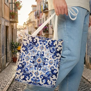 Op de afbeelding: Een draagtas met een blauw en wit bloemenpatroon. De tas wordt door een persoon vastgehouden en heeft witte bandjes. Het ontwerp is geïnspireerd op traditionele Portugese tegels.