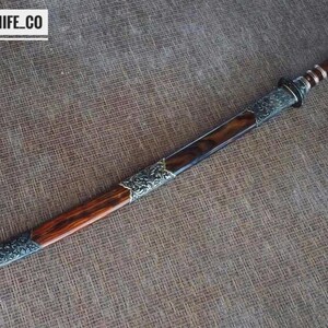 May include: A handcrafted sword with a wooden handle and a silver-coloured blade. The blade is housed in a wooden sheath with silver-coloured decorative accents. The text "BLAYDZ_KNIFE_CO" is in the upper left corner.