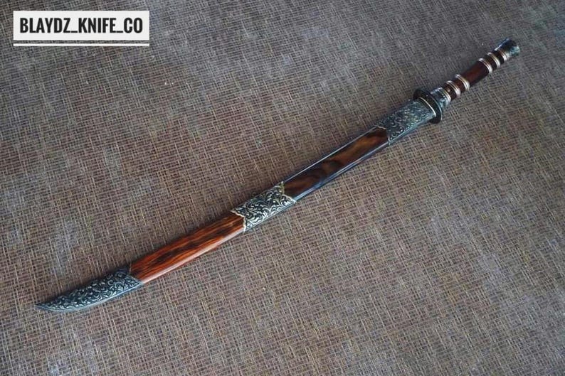 May include: A handcrafted sword with a wooden handle and a silver-coloured blade. The blade is housed in a wooden sheath with silver-coloured decorative accents. The text "BLAYDZ_KNIFE_CO" is in the upper left corner.
