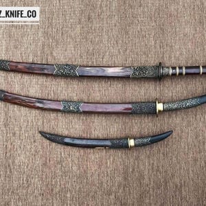 May include: Three decorative swords with ornate handles and blades. The swords have dark brown and black blades with decorative metal accents. The handles are a mix of dark brown and silver. The text "BLAYDZ_KNIFE_CO" is in the top left corner.