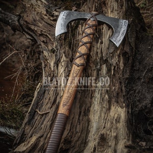 May include: A double-headed axe with a brown leather wrapped handle. The axe is resting on a tree stump with a rough, textured surface. The axe head is made of metal and has a hammered finish.