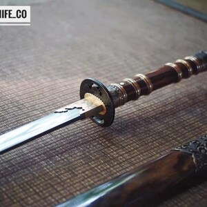 May include: A Japanese-style sword with a dark wooden handle and a silver blade. The handle has a detailed design with a dark brown finish. The scabbard is visible at the bottom. The text "BLAYDZ_KNIFE_CO" is at the top.