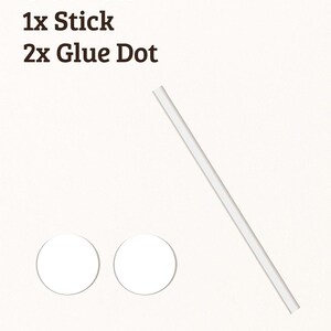 May include: Clear acrylic stick and glue dots. The image shows a clear acrylic stick and two white glue dots. Text on the image reads: Clear Acrylic Stick + Glue Dots, 1x Stick, 2x Glue Dot.