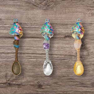 Puede incluir: Tres cucharas de plata con tapas en forma de hongo y detalles de cristal. Los hongos son iridiscentes con colores rosa, azul y verde.