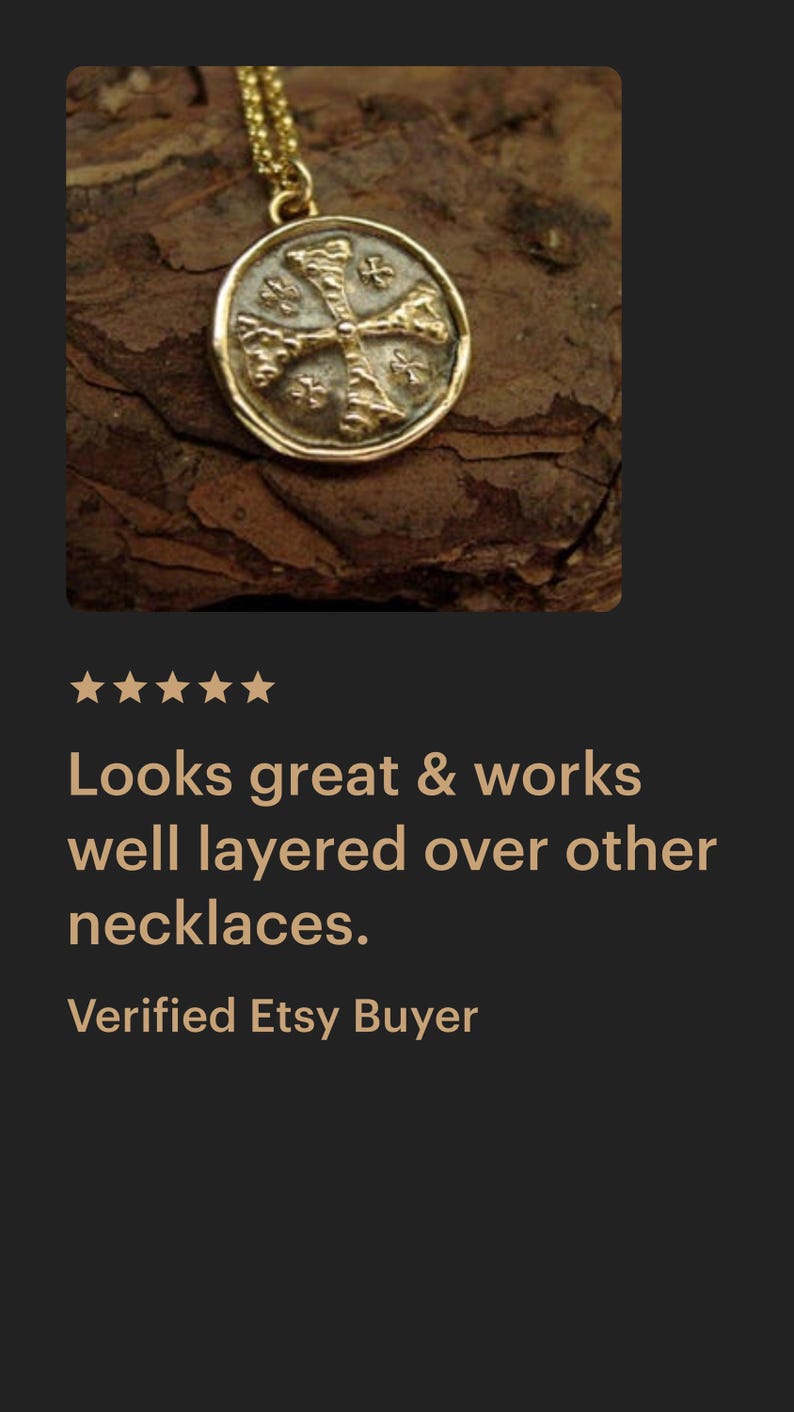 May include: A gold-toned circular pendant necklace featuring a raised cross design with textured details. The pendant is suspended from a delicate gold-toned chain, showcasing a metallic finish and a coin-like shape with a slightly irregular, rounded edge.