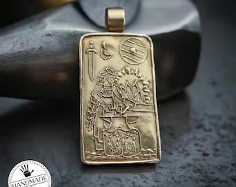 May include: Gold-colored rectangular pendant with a detailed relief of a blacksmith at work, a sword, shield, and crescent moon. The pendant has a loop at the top for a chain. The word "HANDMADE" is printed on a white circle.