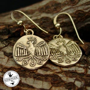 A pair of gold coin earrings with a raised phoenix. A handmade sticker at the lower left corner.