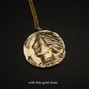 May include: A gold necklace with a round pendant featuring a detailed profile of a woman's face. The pendant is attached to a thin gold chain.