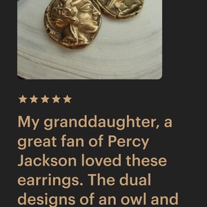 May include: Gold-toned earrings with a coin-like design. One earring features a profile, the other an owl. The earrings are displayed on a white surface. The text in the image says: "My granddaughter, a great fan of Percy Jackson loved these earrings."