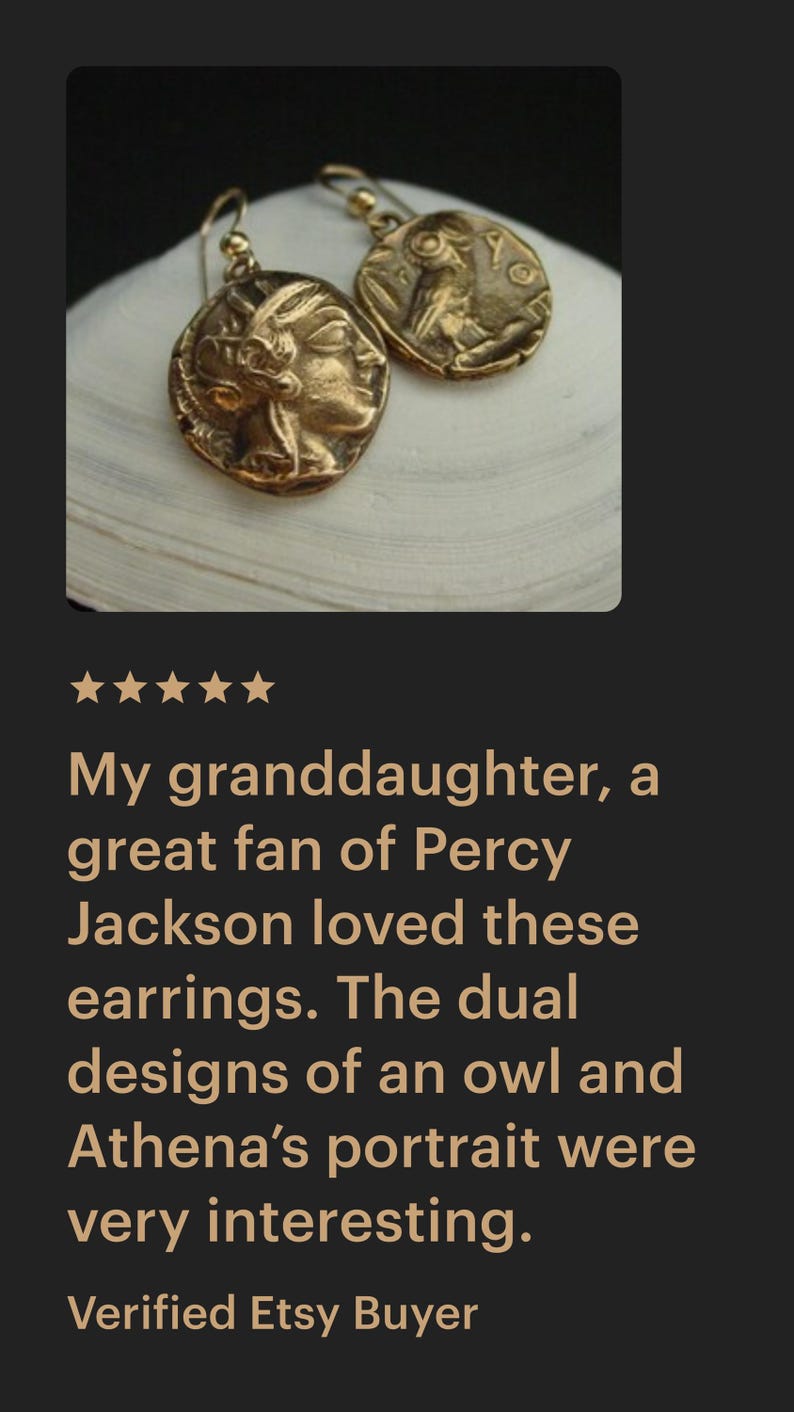 May include: Gold-toned earrings with a coin-like design. One earring features a profile, the other an owl. The earrings are displayed on a white surface. The text in the image says: "My granddaughter, a great fan of Percy Jackson loved these earrings."