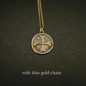 May include: A gold-toned circular pendant featuring a textured cross design with small cross accents in each quadrant, suspended from a thin gold-toned chain. The text "with thin gold chain" is visible at the bottom of the image.