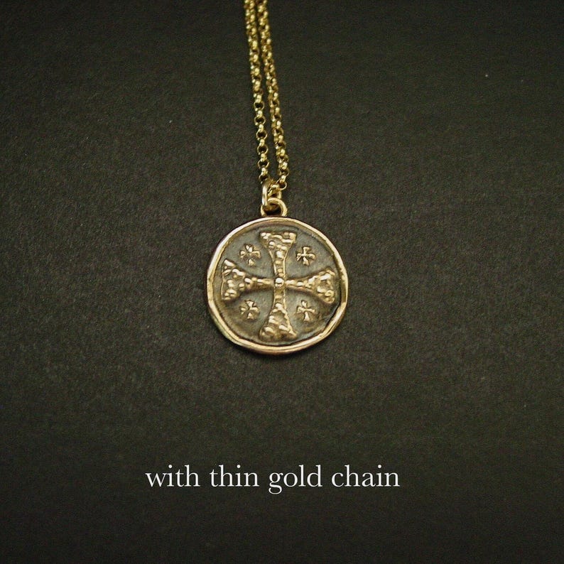 May include: A gold-toned circular pendant featuring a textured cross design with small cross accents in each quadrant, suspended from a thin gold-toned chain. The text "with thin gold chain" is visible at the bottom of the image.