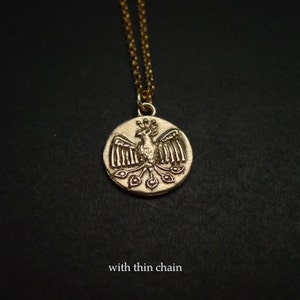 May include: A gold-toned circular pendant necklace featuring a relief design of a bird with spread wings and a fanned tail. The pendant is suspended from a delicate, thin gold-toned chain. The text "with thin chain" is printed at the bottom.