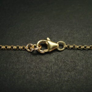 May include: A gold-toned metal chain necklace featuring a lobster claw clasp mechanism. The chain consists of small, uniform circular links connected in a continuous row, with the clasp secured at the centre to join the two ends of the necklace.