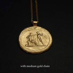 May include: Gold-colored pendant necklace with a medium gold chain. The pendant features a detailed relief of classical figures. The necklace is displayed against a dark background. The text "with medium gold chain" is at the bottom.