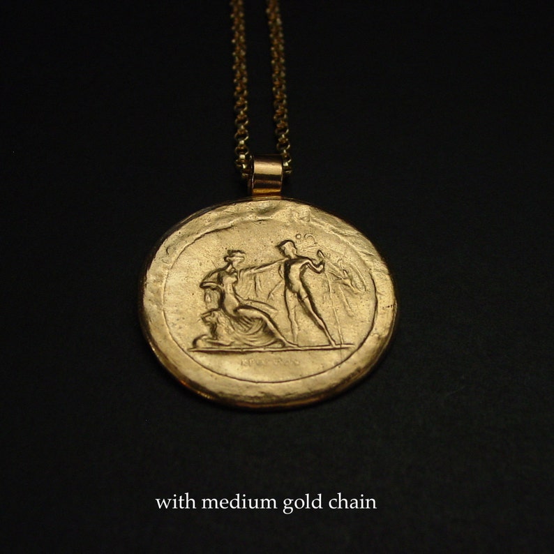 May include: Gold-colored pendant necklace with a medium gold chain. The pendant features a detailed relief of classical figures. The necklace is displayed against a dark background. The text "with medium gold chain" is at the bottom.