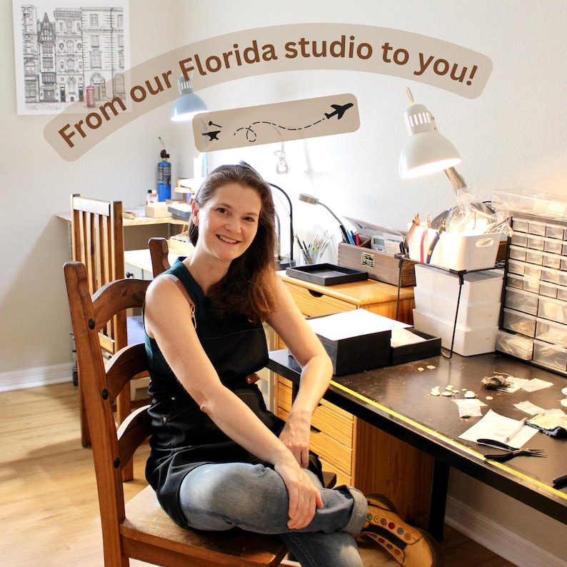 May include: A person wearing a dark green apron and blue jeans sits at a wooden desk in a studio. The desk features a white lamp, a multi-drawer storage unit, and various tools. Text above reads: From our Florida studio to you! with an icon.