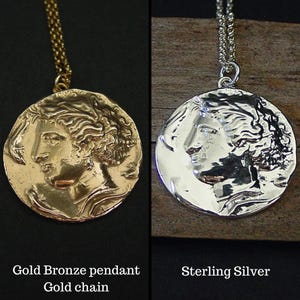 May include: Two versions of a round pendant necklace featuring a profile of a woman's face. The pendant on the left is gold bronze with a gold chain. The pendant on the right is sterling silver with a silver chain.  Gold Bronze pendant, Gold chain, Sterling Silver.