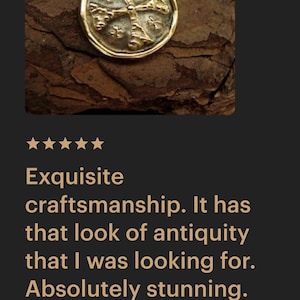 May include: A gold-toned circular pendant necklace featuring a raised cross design with textured, weathered detailing on the surface. The pendant is suspended from a delicate gold-toned chain, showcasing a metallic finish with a worn, aged appearance.