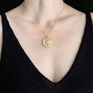 May include: A gold chain necklace with a large, round pendant featuring a profile of a woman's face. The pendant is a detailed, embossed design.