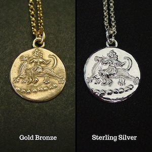 May include: A gold bronze pendant necklace and a sterling silver pendant necklace, both featuring a circular coin design with a relief of a figure riding a mythical creature. Each pendant hangs from a matching metal chain, with text labels.