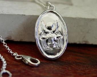 May include: A silver-toned oval pendant necklace featuring a raised relief design of a bull head with prominent horns. The pendant is attached to a delicate silver-toned chain with a lobster claw clasp, showcasing a polished metallic finish.