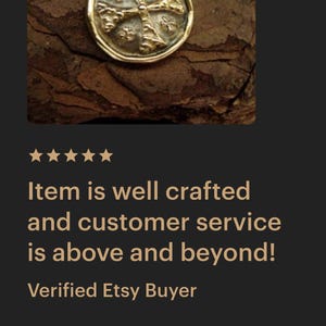 May include: A gold-toned circular pendant necklace featuring an embossed cross design with textured details. The pendant is suspended from a delicate gold-toned chain, showcasing a metallic finish and a distinct, raised cross motif on its face.